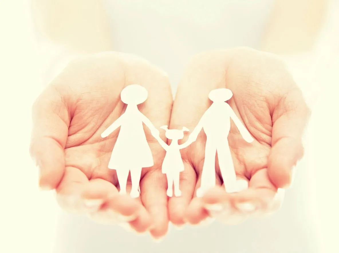 A paper-cut family of a mother, a child and a father held in two cupped hands.