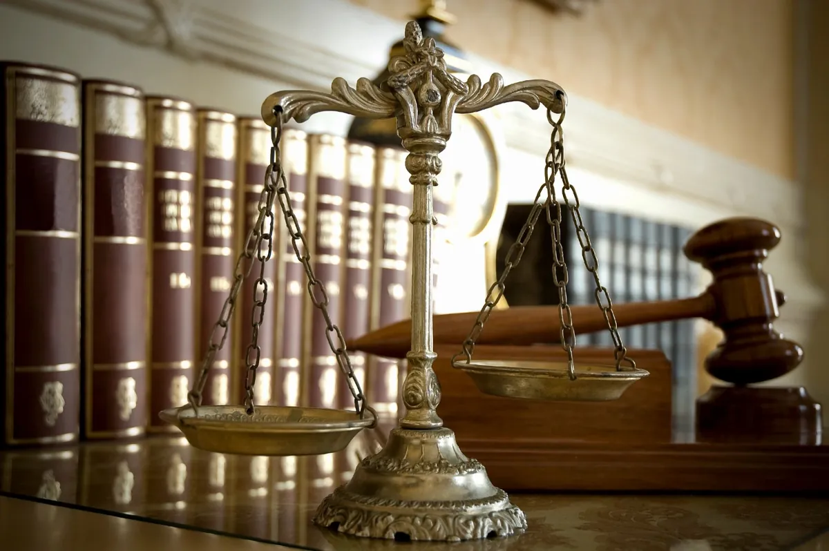 A brass balance scale and a wooden gavel in front of shelves of law books