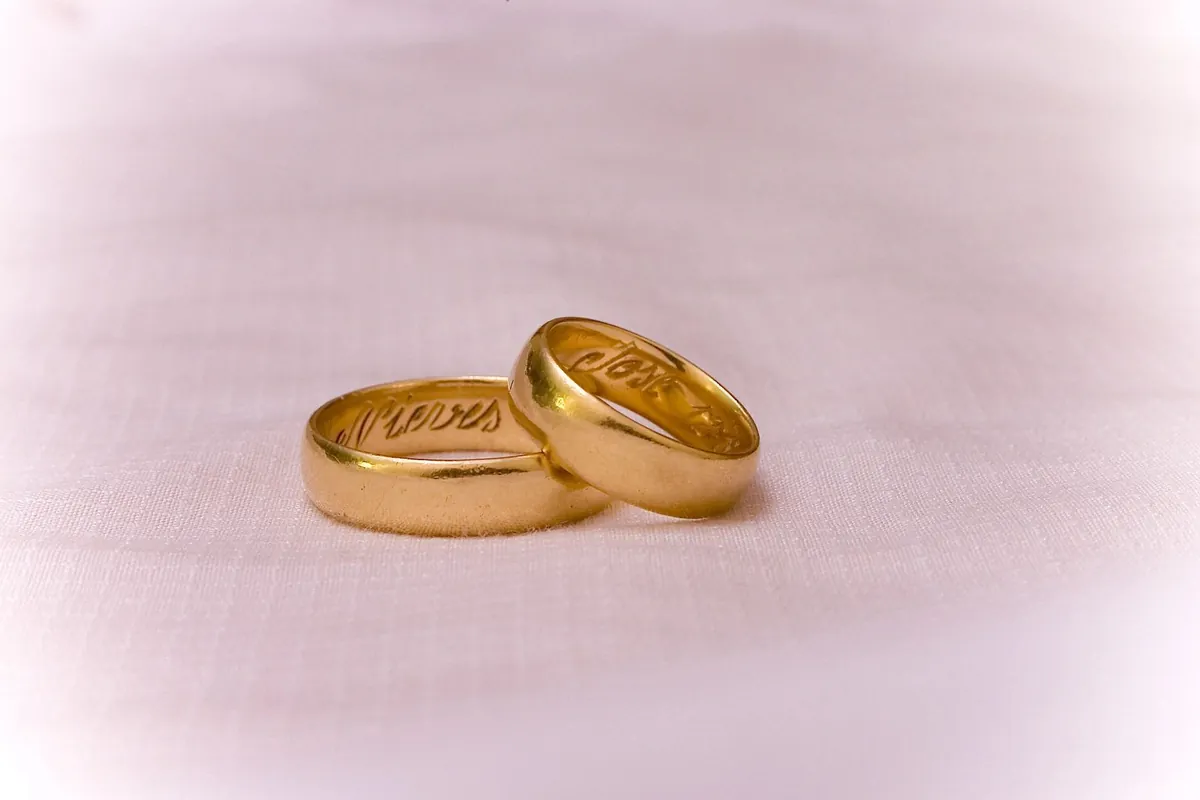 Two gold wedding rings lying side by side on pale pink fabric.