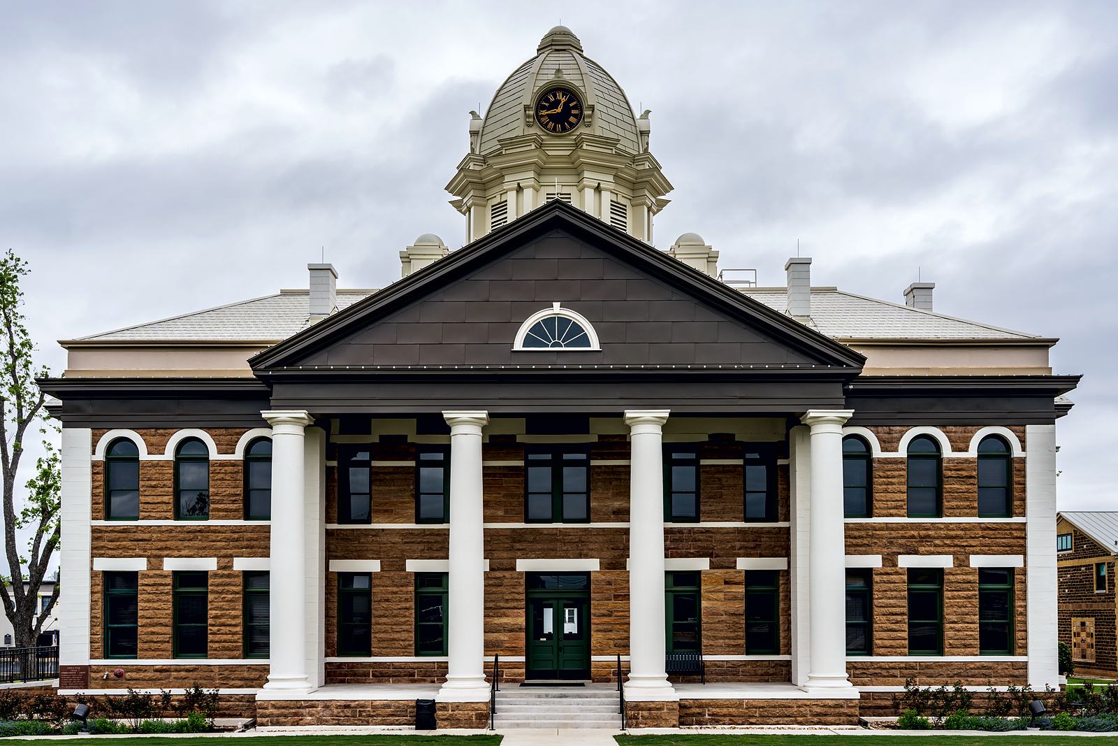 Front of the Mason County Courthouse in Texas, a sandstone building with white columns, a pediment and a clock cupola, under an overcast sky.