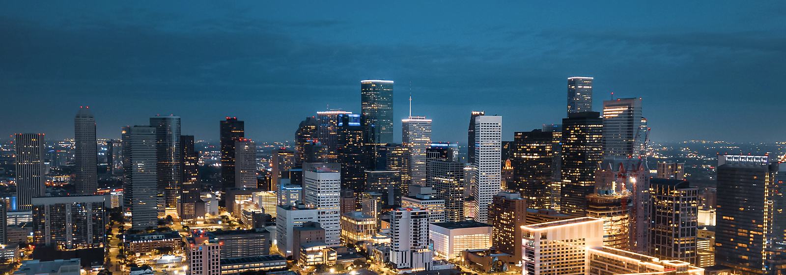 Downtown Houston's towers at blue hour, lit from within.