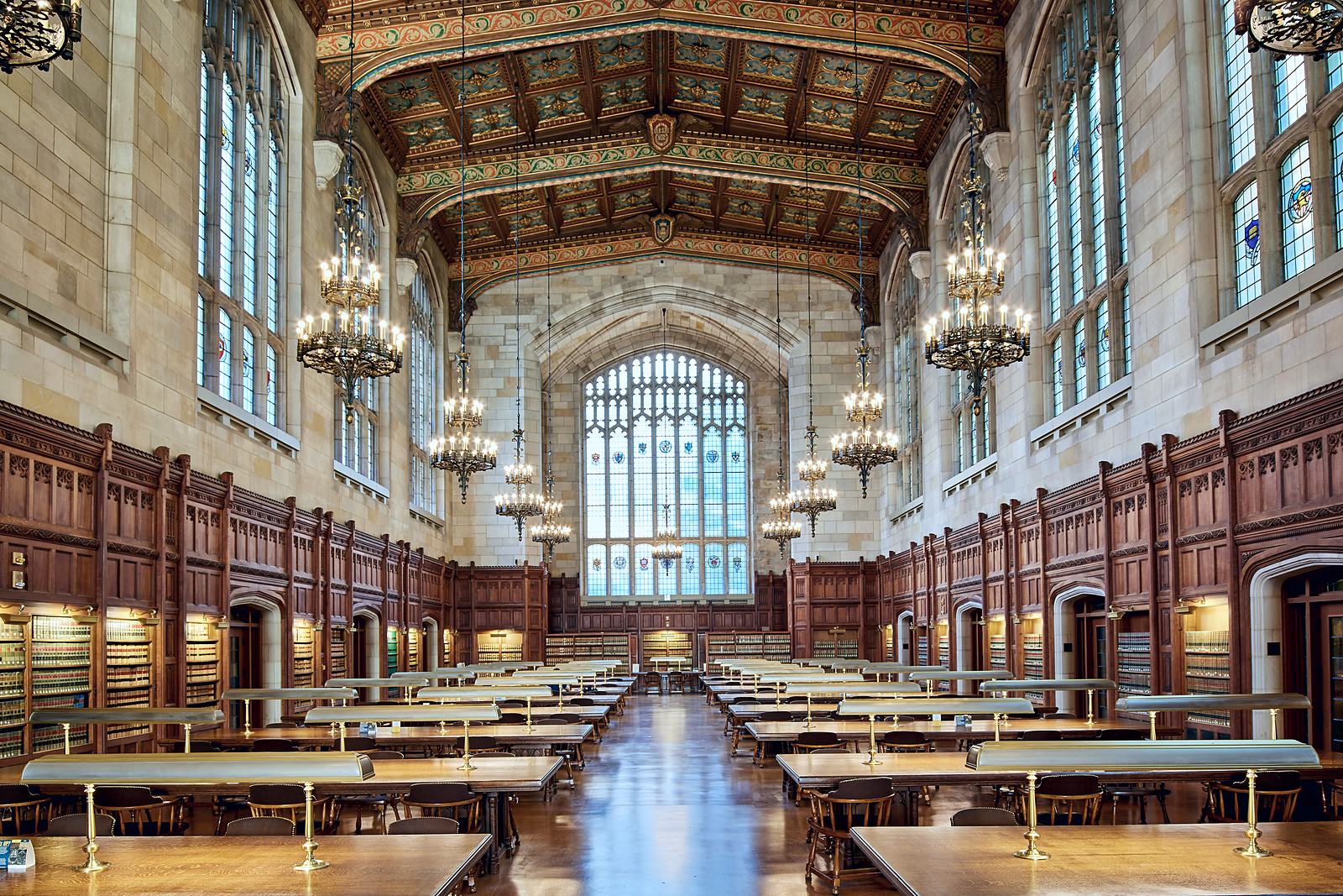 An empty law library reading room with long wooden tables, reading lamps and chandeliers.