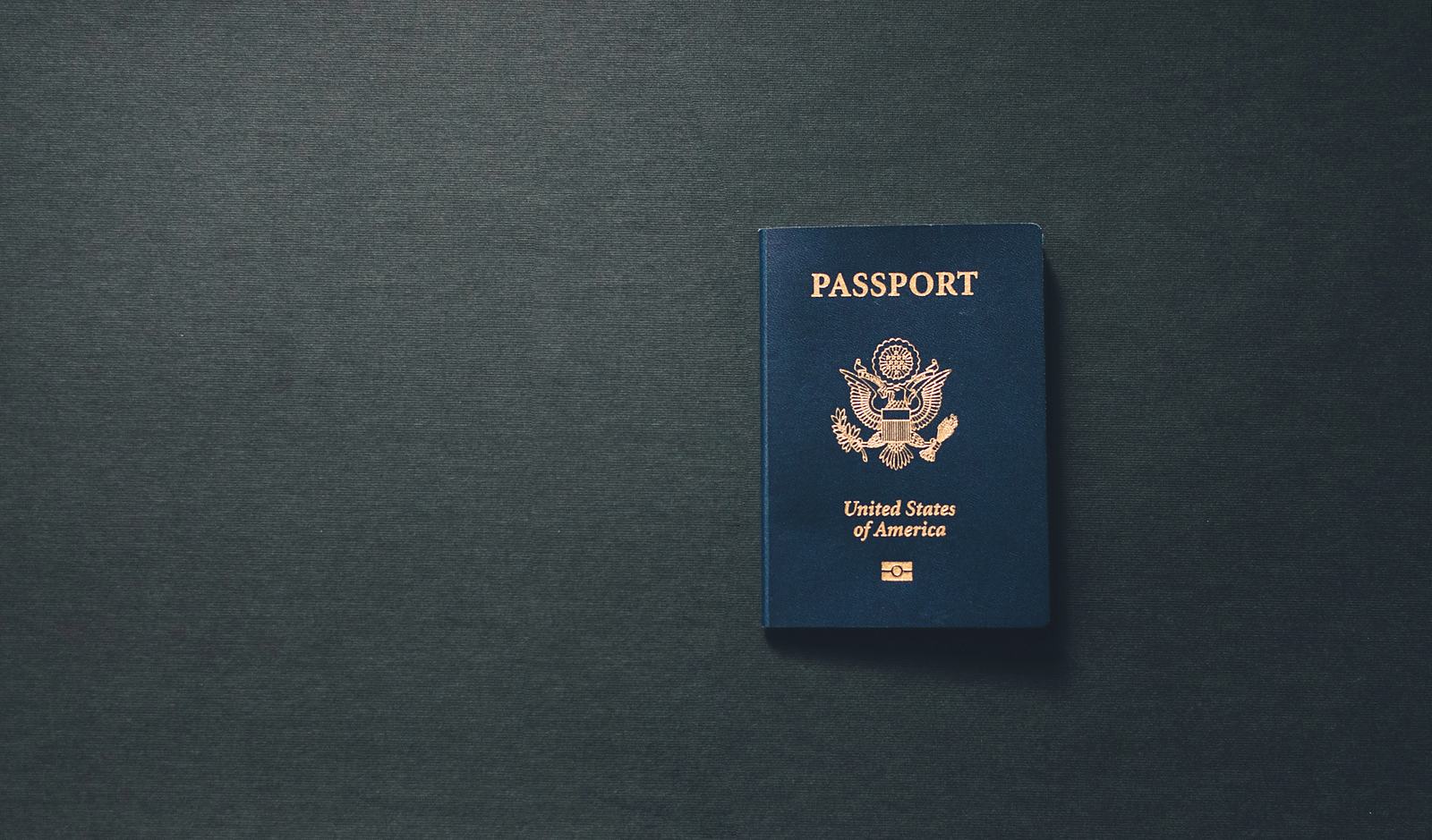A closed U.S. passport lying alone on a dark grey surface.