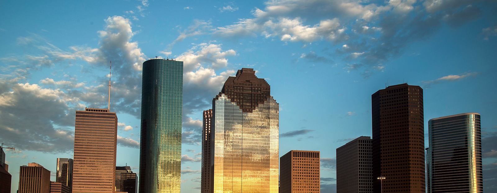 Downtown Houston's office towers in golden evening light, with a glass tower reflecting the sun.